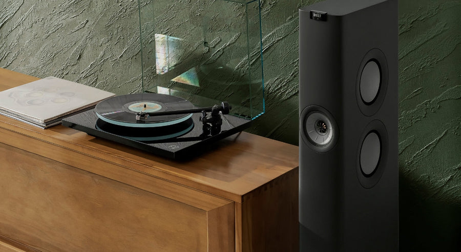KEF floorstanding HiFi speaker positioned next to a turntable on a wooden media unit in a modern living room