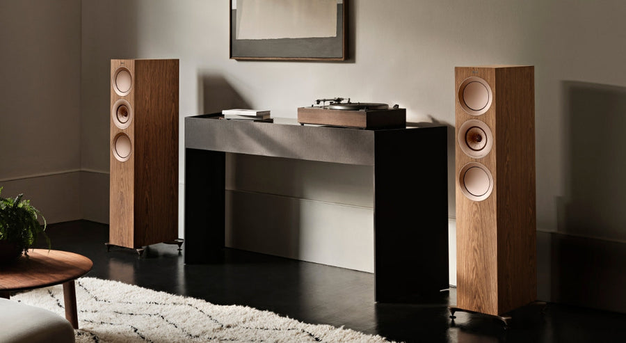 KEF floorstanding speakers in a natural wood finish paired with a vinyl turntable on a minimalist black console table, set in a modern listening room.