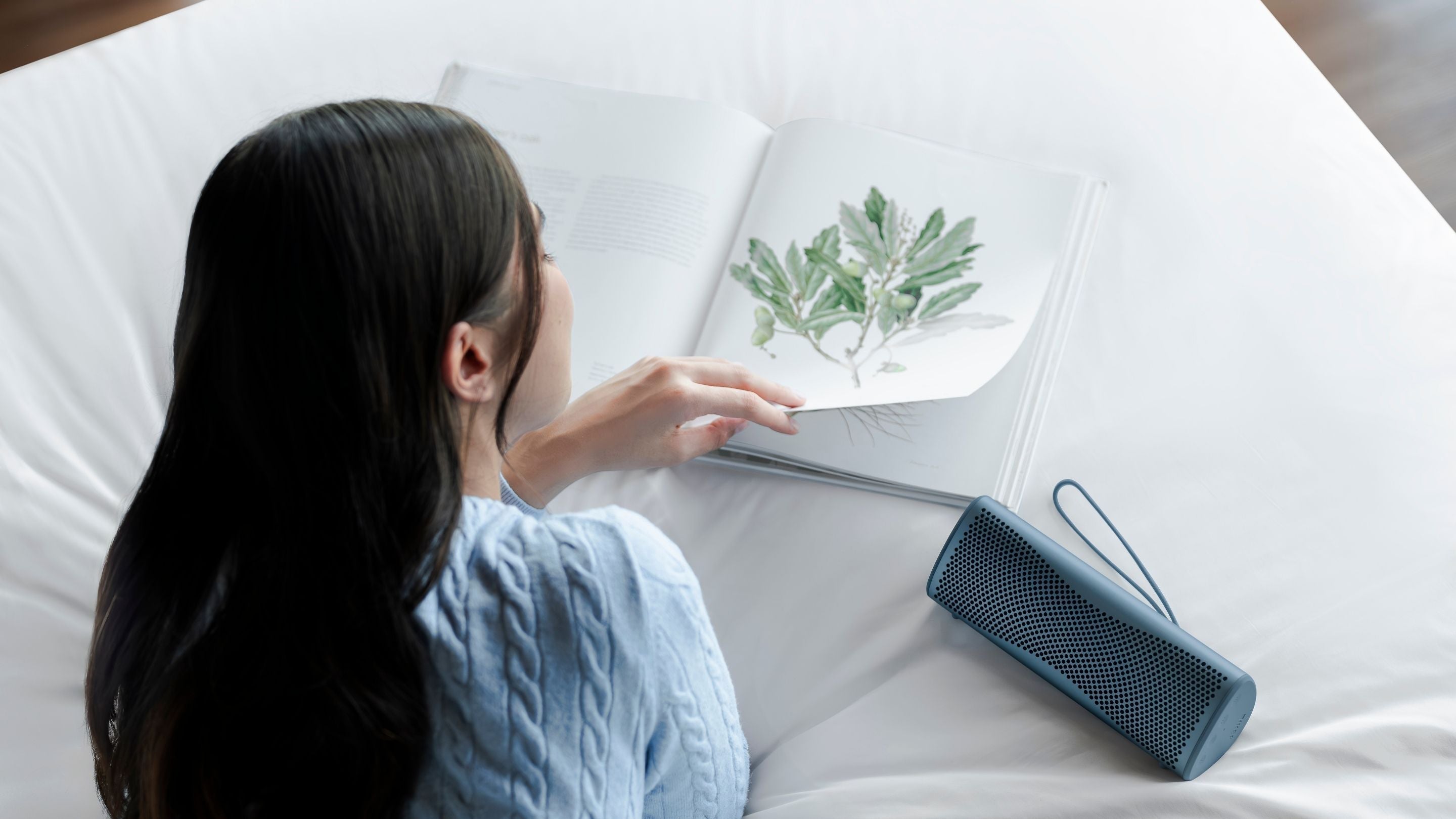 A girl reading a book next to a KEF Muo Bluetooth speaker