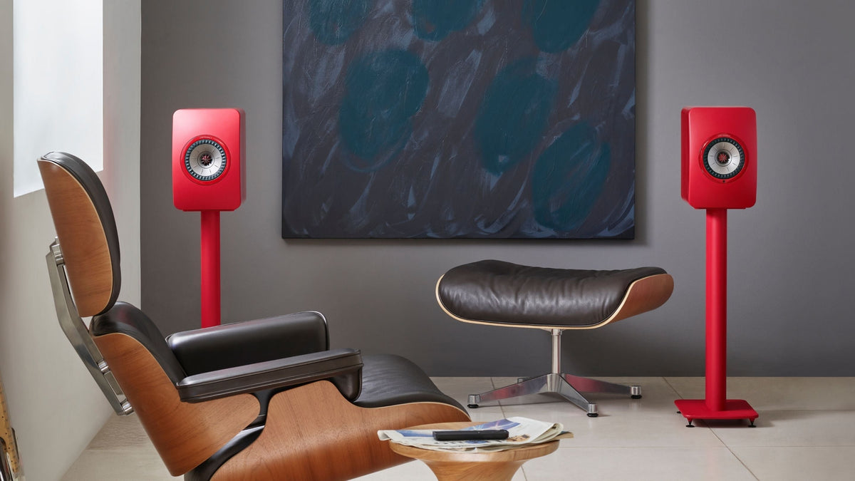 LS50 Wireless II Red speakers on stands in a modern room with a chair and abstract painting.