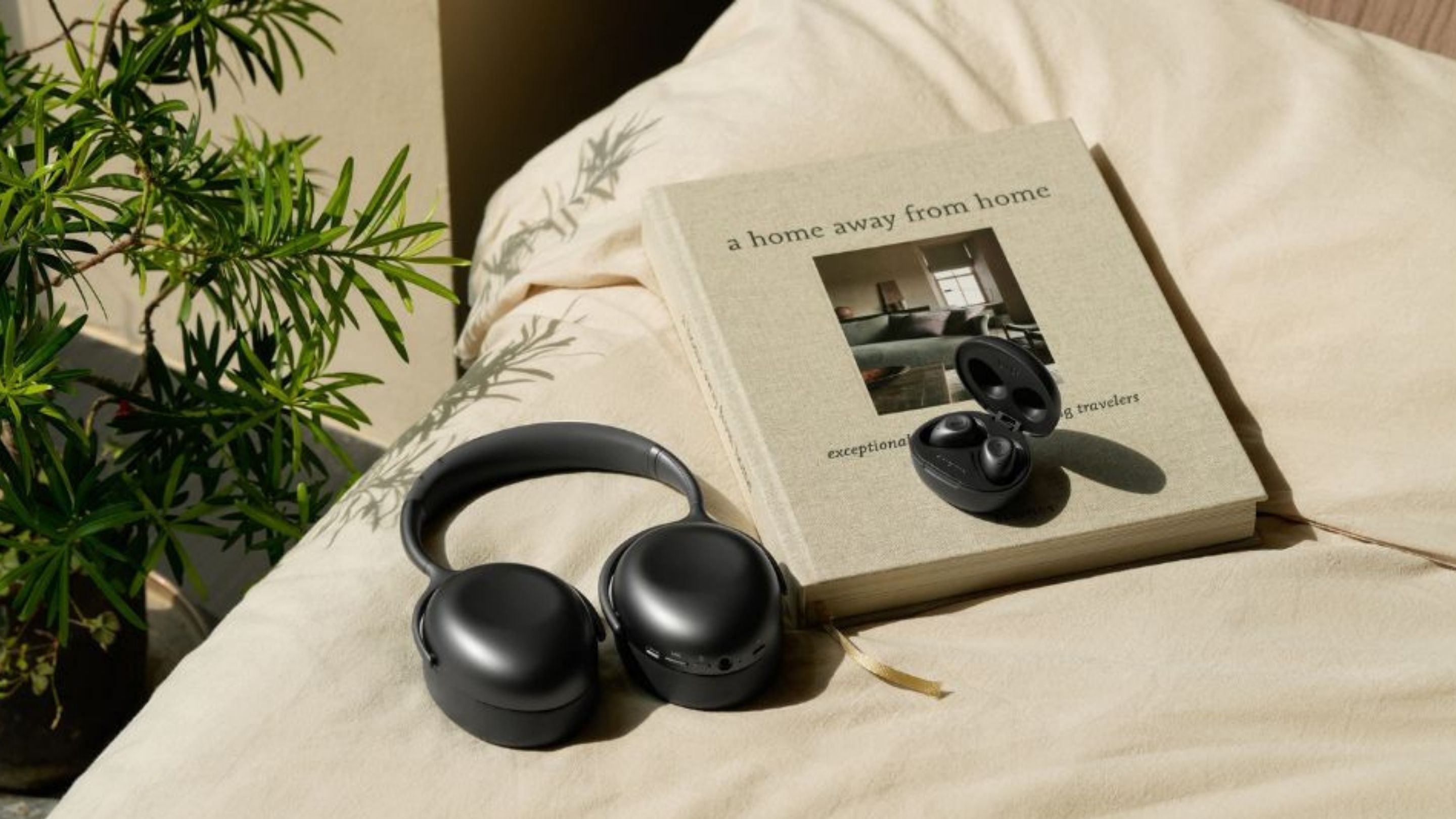 Mu7 & Mu3 headphones on a book titled 'A Home Away from Home' on a light surface with a plant in the background.