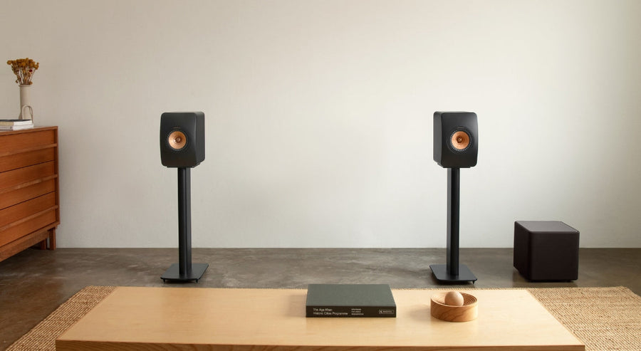 KEF bookshelf speakers on stands with compact black subwoofer in a minimalist modern living room