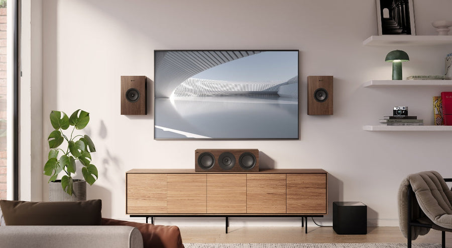 Stylish home entertainment setup featuring KEF Q Series walnut speakers, a centre channel speaker, and subwoofer, arranged around a wall-mounted TV in a modern living room with Scandinavian-inspired decor.